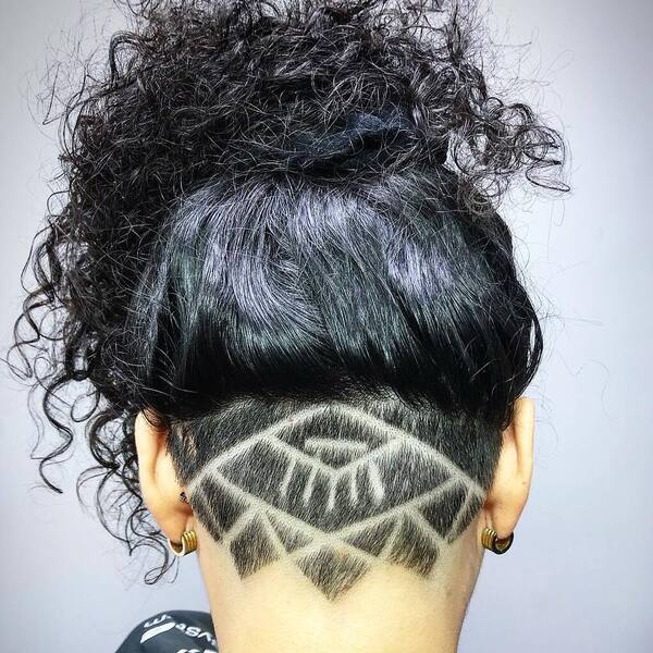 Nape Undercut Design with Raven Black Hair and Messy Bun- a woman wearing a pair of earrings