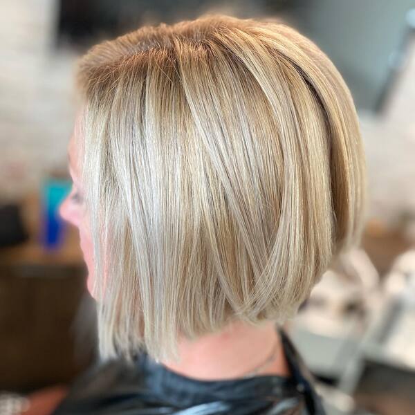 Short Bob with Creamy Blonde- a woman wearing a black barber's cape