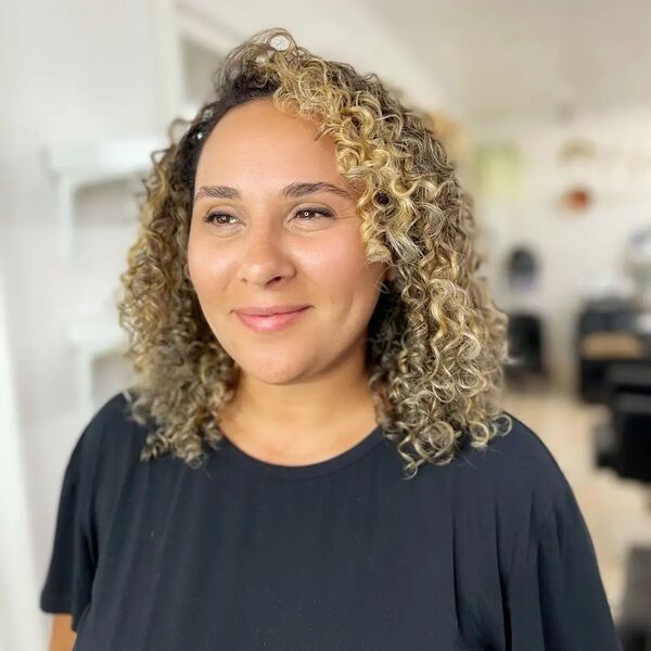 Shoulder Length Kinky Curls with Balayage Blonde- a woman wearing a black blouse