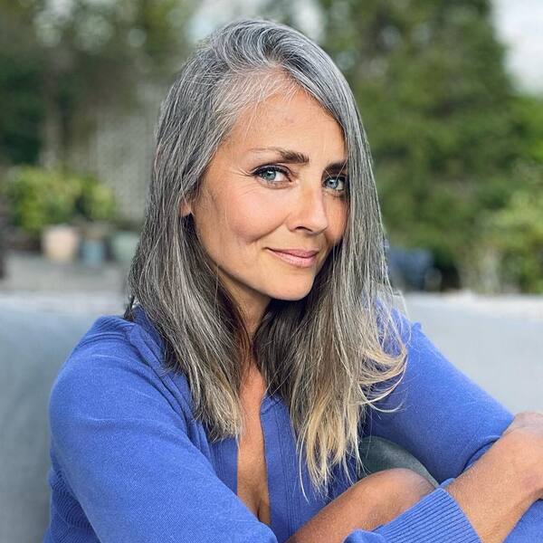 Brown Long Hairstyle for Growing Out Gray Hair- a woman with gray hair wearing a blue sweater