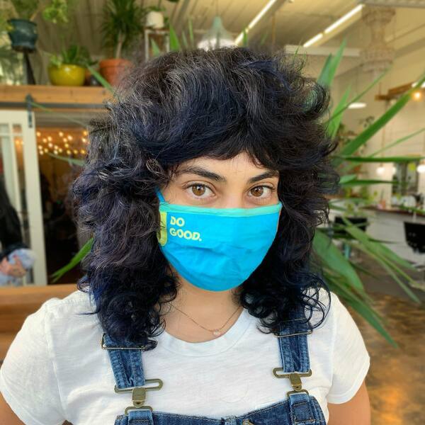 Curly Shag Haircut- a woman wearing a blue face mask and a denim jumper suit