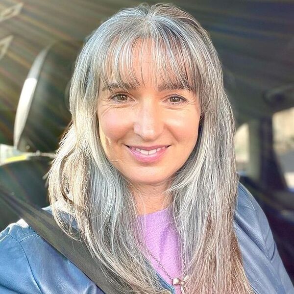 Feathered Hairstyles for Natural Gray Hair- a woman with gray hair wearing a blue leather jacket