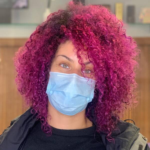 Pink Hair Color with Puffy Curls- a woman wearing a face mask and a black jacket