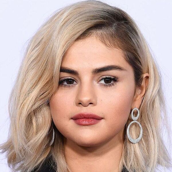 Selena Gomez Haircut for Round Faces- Selena Gomez wearing a black leather suit and a pair of big earrings